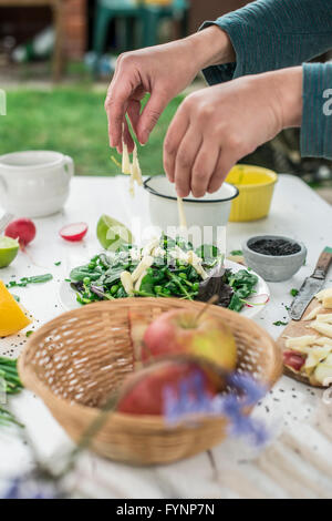 Hinzufügen von zerkleinerten Äpfel. Salat von jungem Spinat, Kresse, Radieschen, Schnittlauch, Apfel und schwarzem Sesam. Dressing aus Kalk und Sesam o Stockfoto