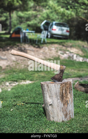 AX auf einem Baumstumpf im Wald stecken. Zelt und Auto auf Hintergrund Stockfoto