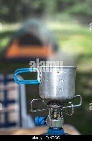 Tourist-Cup am Gasherd im Wald. Zelt auf Hintergrund. Stockfoto