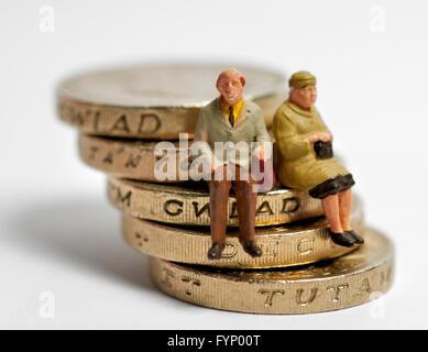 Zwei Miniatur Figur Rentner sitzen auf einem schiefen Stapel von 1 Pfund-Münzen Stockfoto