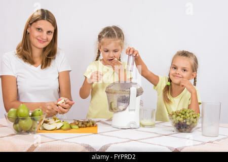 Mädchen nagt Birnen, bis Mutter und Schwester in einem Entsafter Saft gepresst Stockfoto