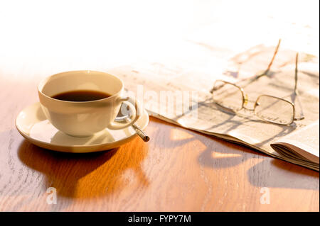 Tasse Kaffee, mit Zeitungspapier und Gläser, auf einem sonnigen Morgen. Stockfoto