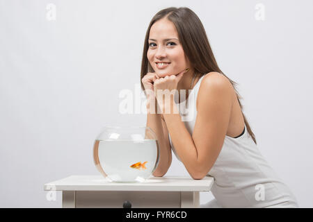 Das Mädchen sitzt nahe dem Aquarium mit Goldfischen und sieht auf dem Bild Stockfoto