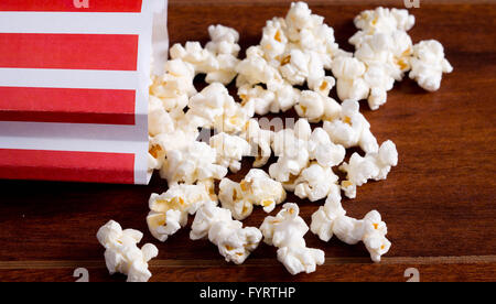 Rot weiß gestreiften Container-Box liegen kippte auf Holzoberfläche mit Popcorn verteilt Stockfoto