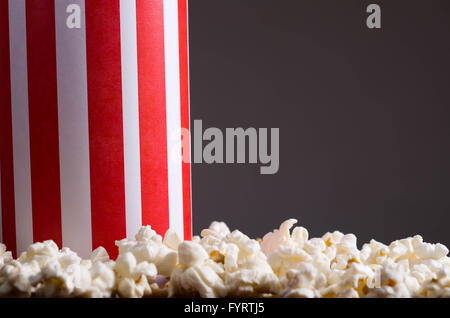 Closeup rot weiß gestreift Container-Box stehend mit Popcorn herumliegen, niedrigen Winkel, grauen Hintergrund Stockfoto