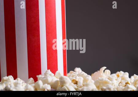 Closeup rot weiß gestreift Container-Box stehend mit Popcorn herumliegen, niedrigen Winkel, grauen Hintergrund Stockfoto