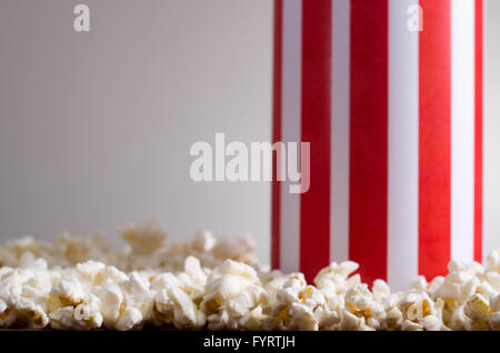 Closeup rot weiß gestreift Container-Box stehend mit Popcorn herumliegen, niedrigen Winkel, grauen Hintergrund Stockfoto