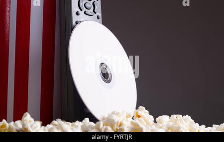 Closeup rot weiß gestreift Container mit Popcorn herumliegen, DVD-Disc und Fernbedienung stützte sich auf Box, niedrigen Winkel, grauen Hintergrund stehend Stockfoto