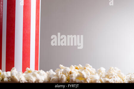 Closeup rot weiß gestreift Container-Box stehend mit Popcorn herumliegen, niedrigen Winkel, grauen Hintergrund Stockfoto