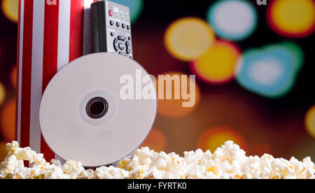 Closeup rot weiß gestreift Container mit Popcorn herumliegen, DVD-Disc und Fernbedienung stützte sich auf Feld, niedrigen Winkel, auffällige lebendige Lichter Hintergrund stehend Stockfoto