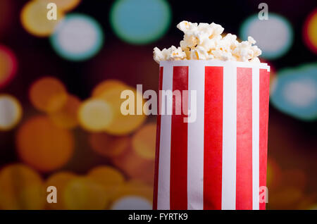 Closeup rot-weiß gestreiften Container mit Popcorn über Edge, niedrigen Winkel, auffällige lebendige Lichter Hintergrund stehend Stockfoto