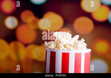 Closeup rot-weiß gestreiften Container mit Popcorn über Edge, niedrigen Winkel, auffällige lebendige Lichter Hintergrund stehend Stockfoto