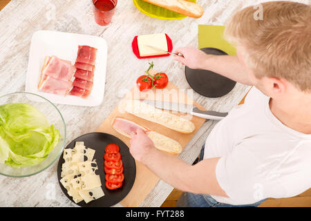 Junger Mann bereitet einen Sandwich Stockfoto