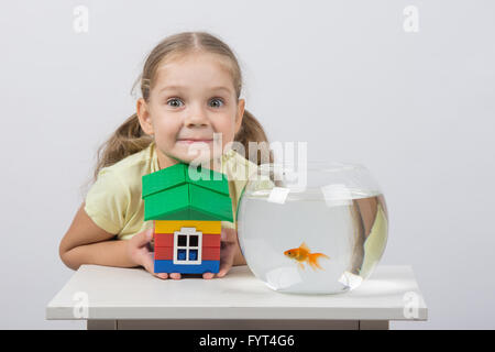 Vierjährige Mädchen hält ein Spielzeug Haus und sitzt vor der einen Goldfisch Stockfoto