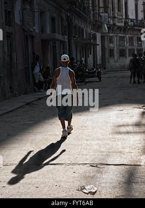 Ein Mann zu Fuß von der Sonne in den Schatten. Er ist das Rauchen einer Zigarette. Im Hintergrund ist ein Motorrad und Seitenwagen und halb verfallenen Gebäuden. Stockfoto