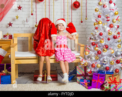 Auf der Bank sitzt ein Mädchen in eine Mütze und Handschuhe von Santa Claus, das andere Mädchen trug einen Beutel auf dem Kopf Stockfoto