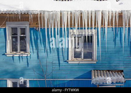 Gefährliche Eiszapfen hängen vom Dach eines Holzhauses Stockfoto