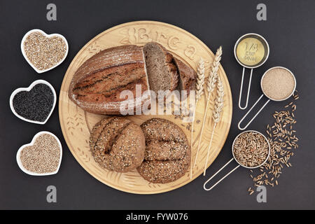 Hausgemachtes Roggenbrot Laib und bestreute Brötchen auf einem Holzbrett mit Haferflocken, Mohn und Sesam Samen im Herzen geformte Schalen. Stockfoto