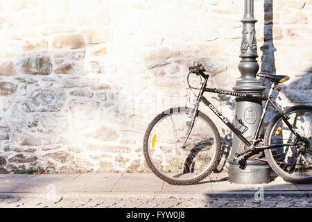 Fahrrad auf einen Laternenpfahl in der Sonne Gießen Schatten auf der Steinmauer gelehnt Stockfoto