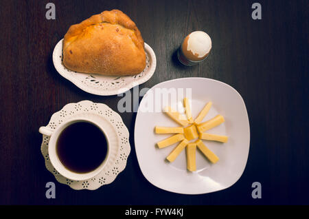 Latein inspiriert Frühstück am dunklen Holztisch einschließlich Käsescheiben auf weiße quadratische Platte neben Glas Orangensaft, Kaffee, gekochtes Ei und ein Empanada Brot gelegt Stockfoto