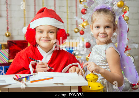 Mädchen verkleidet als Weihnachtsmann Schreiben eines Briefes, stehen neben einer Fee mit einer Taschenlampe in der hand Stockfoto