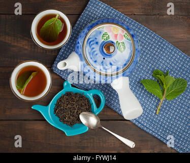 Ganze Blatt-Tee mit Teekanne und zwei Tassen auf Handtuch und hölzernen Hintergrund. Ansicht von oben. Stockfoto