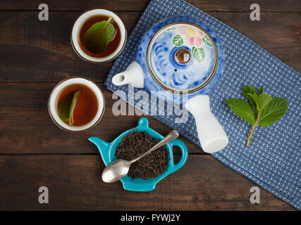 Ganze Blatt-Tee mit Teekanne und zwei Tassen auf Handtuch und hölzernen Hintergrund. Ansicht von oben. Stockfoto