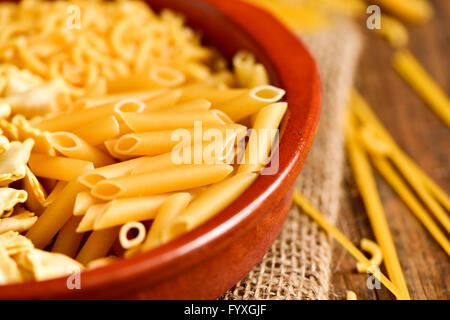 Nahaufnahme von einem Steingut-Schale mit verschiedenen Teigwaren wie Ravioli, Spaghetti oder Mostaccioli, auf einem rustikalen Holztisch Stockfoto