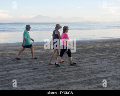 Drei Touristen zu Fuß am Strand in den frühen Morgenstunden in Jimbaran Bay, Bali. Stockfoto