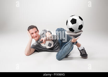 Das Porträt des Lüfters mit Ball, halten tv remote auf grauem Hintergrund Stockfoto