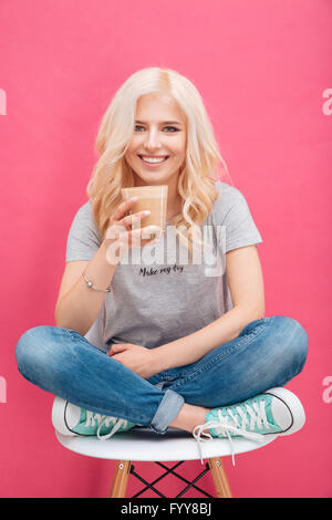 Lächelnde junge Frau trinken Cappuccino und Blick in die Kamera über rosa backgroud Stockfoto