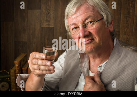 Graue älterer Mann einen Genever-Drink in einem Schnapsglas Stockfoto