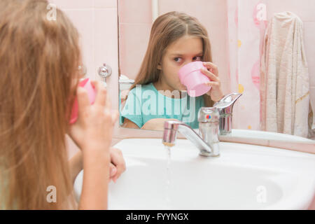 Mädchen wählt das Wasser im Mund aus der Tasse durch Spülen den Mund nach dem Zähneputzen Stockfoto