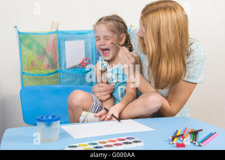 Mutter kitzelt die Wange mit einem Pinsel, seine Tochter, fünf Jahre zu malen Stockfoto