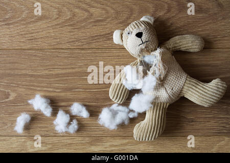 Eine traurige, verlassenen Teddybär mit seiner Füllung herausgezogen und in einem dunklen, hölzernen Fußboden verstreut. Stockfoto