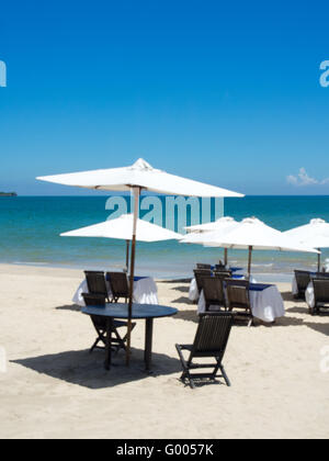 Holztische und Stühle set unter weißen Sonnenschirmen am Strand. Stockfoto