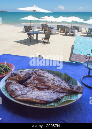 Chargrilled Snapper Fisch auf eine weiße Platte und Banane lassen in einem Restaurant am Strand präsentiert. Stockfoto