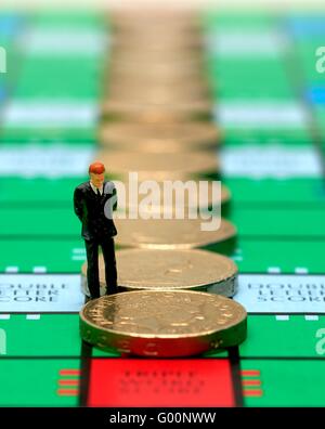 Ein Miniatur-Business-Mann in einem Anzug mit Blick auf einige Pfund-Münzen Stockfoto