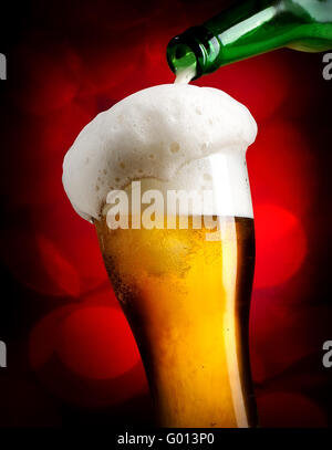 Bier aus der Flasche in Glas gießen, auf rotem Grund Stockfoto