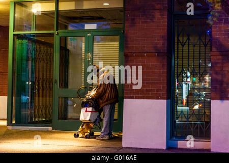 Ein älterer Obdachloser Mann mit seinen Habseligkeiten auf einer Straße in San Francisco nach Einbruch der Dunkelheit. Stockfoto