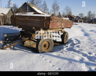 Verlassene rostigen landwirtschaftliche Anhänger unter Schnee im russischen Dorf Stockfoto