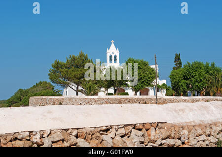 Menorca, Balearen, Spanien, Europa: eine Mauer aus Stein und eine weiße Kirche in der Landschaft Menorcas Stockfoto