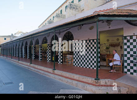 Menorca, Balearen, Spanien, Europa: ein Metzger unter den Arkaden des Platzes Plaza de la Libertad in Ciutadella sitzt Stockfoto