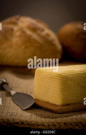 Hand aufgewühlt selbst gemachter Butter auf hölzernen Paddel mit Buttermesser und Brot. Stockfoto