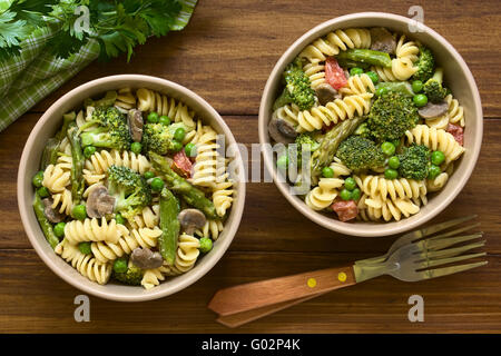 Pasta Primavera mit grünem Spargel, Erbsen, Brokkoli, Pilzen und Tomaten in Sahnesauce in Schalen serviert Stockfoto