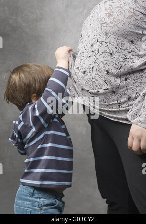 Kleiner Junge guckt unter seine schwangere Mutter blo Stockfoto