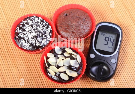 Blutzuckermessgerät und hausgemachte leckere frisch gebackene Schokolade Muffins in rot Silikon Cups, Konzept für Diabetes und dessert Stockfoto