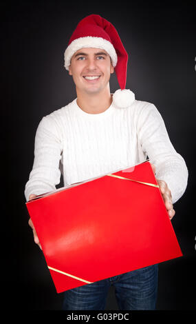 Lächelnd Mann in Weihnachtsmütze gibt ein rotes Kästchen im studio Stockfoto