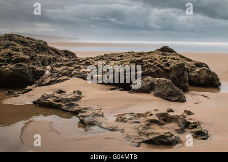 Felsen am Sandstrand im Vordergrund. Windigen Herbsttag mit vielen Wolken. Gewässern des Atlantischen Ozean im Hintergrund. Moula Stockfoto