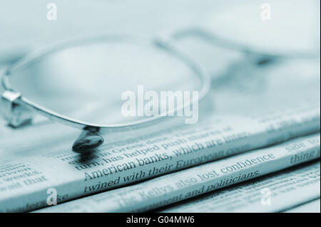 Brille liegen auf einem Stapel Zeitungen. Blau getönt Stockfoto